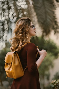 selective focus photography of woman wearing red 3/4-sleeved dress and brown leather bucket bag thumbnail