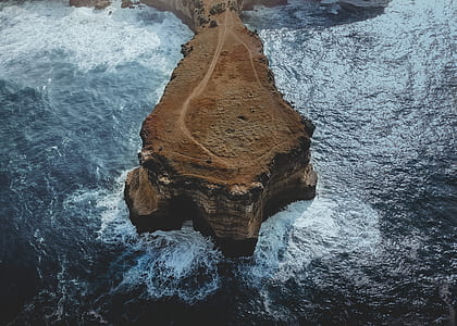 aerial photo of brown rock formation surrounded by body of water thumbnail
