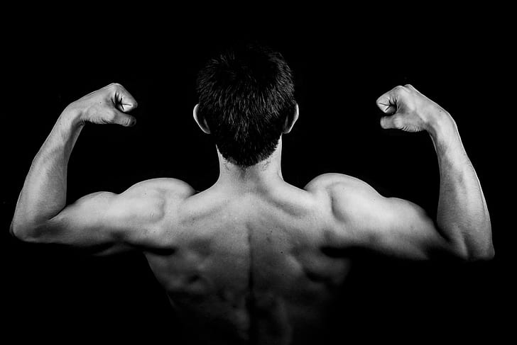 man flexes biceps on dark room