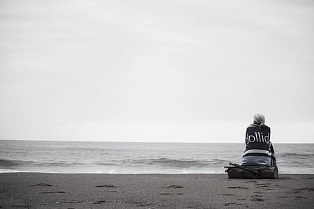 person sitting on driftwood along the shore thumbnail