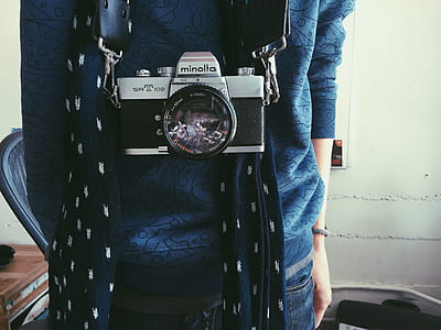 person in blue shirt carrying black Minolta MILC camera on neck thumbnail