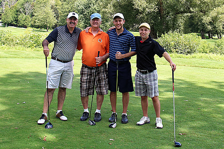 four men standing on green grass field holding golf club thumbnail
