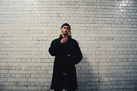 man standing beside beige wall thumbnail