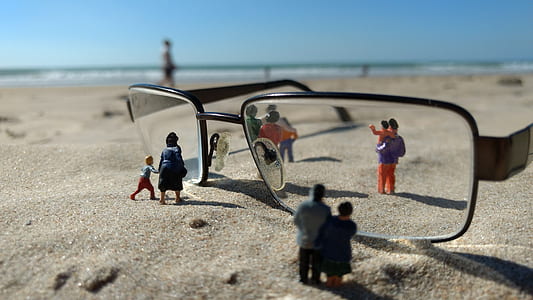depth of field photography of eyeglasses with people figurines on sand thumbnail