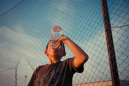 boy drinking water bottle beside fence thumbnail