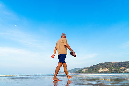 man wearing brown t-shirt and blue shorts walking on seashore during daytime thumbnail