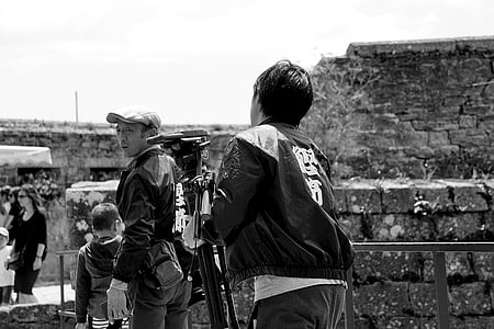 grayscale photo of man holding camera with tripod thumbnail
