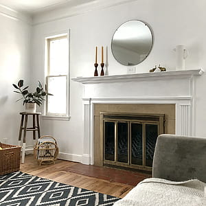 round frameless wall mirror above white wooden fireplace mantle with brass-colored fireplace frame thumbnail