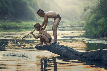 photo of two boys standing on rock on top of body of water thumbnail