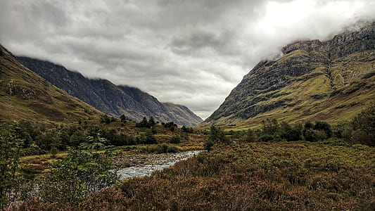 green leaf trees near brown rock formations under nimbus clouds at daytime thumbnail