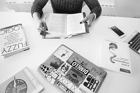 Grayscale Photo of Person Sitting Near Table With Books thumbnail