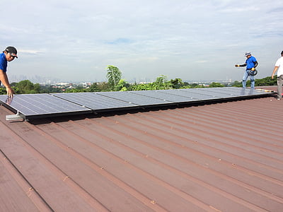 several men installing rectangular black solar panel on top of brown roof at daytime thumbnail