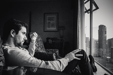 man sitting on sofa chair while staring through the window grayscale photo thumbnail