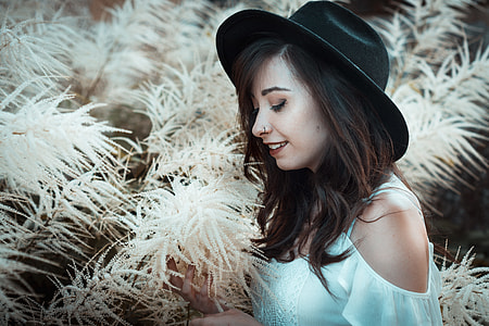 woman wearing white cold-shoulder top and black hat holding flower thumbnail