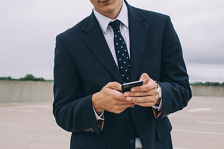 man wearing blue notched lapel suit jacket holding smartphone thumbnail