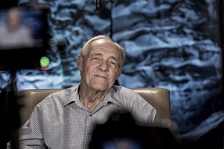 man wearing gray collared top sitting on brown chair thumbnail
