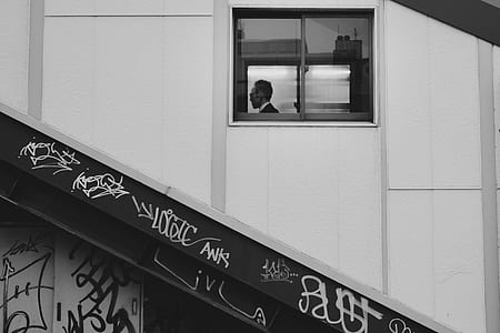 grayscale photo of man sitting beside window inside building thumbnail