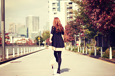 woman in black dress walking at the center of pavement road during day time thumbnail