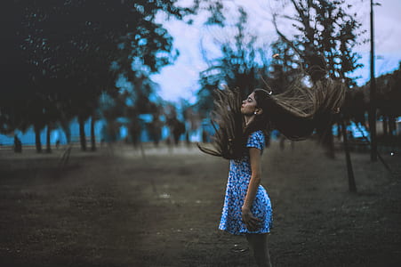 woman in blue dress whipping her hair near brown trees during windy season thumbnail