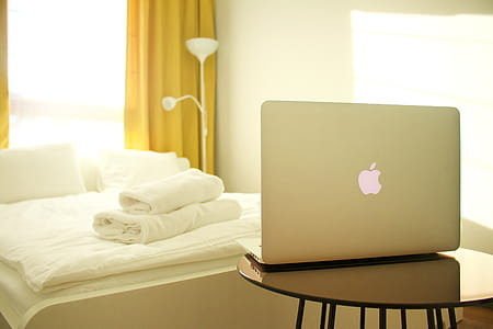 Macbook Air on Top of Wooden Table Facing White Bed thumbnail