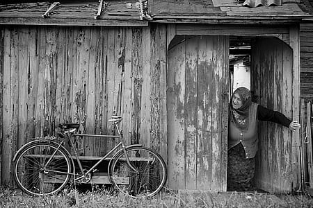 grayscale photo of a woman opening a door watching the bicycle thumbnail