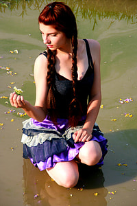 woman kneeling in pond holding white petal flower thumbnail