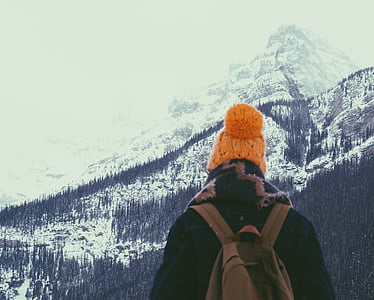 person carrying backpack standing while facing snow capped mountain thumbnail