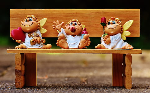 three angel figurines sitting on brown wooden bench in closed-up photo thumbnail