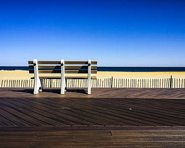 Brown-and-white Wooden Bench Facing Body of Water Under Clear Blue Sky thumbnail