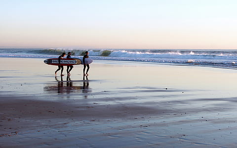 three people carrying surfboards on seashore thumbnail