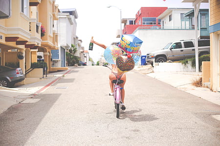 woman riding on bicycle holding green glass bottle thumbnail