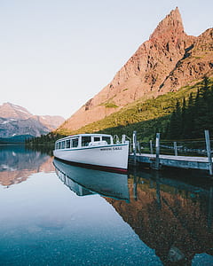 white motor boat on body of water near mountain during daytime thumbnail