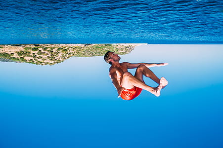 man wearing red shorts diving on water during daytime thumbnail