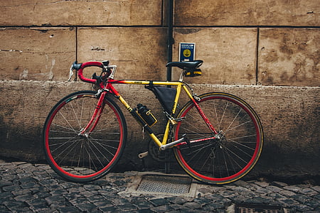 yellow and red road bike parked on brown wall thumbnail