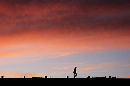 silhouette of man walks on bride during orange clouds thumbnail