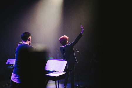man raising hand on stage behind man playing instrument thumbnail