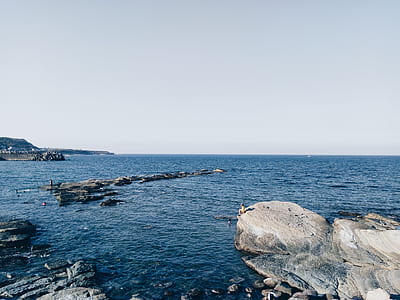 gray cliff beside sea under clear blue sky thumbnail