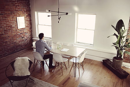 man in long-sleeved shirt reading book while sitting beside dining table thumbnail