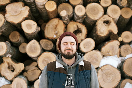 selective focus photography of man standing in front of tree logs thumbnail