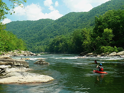 kayaker on red kayak on wild water in between trees at daytime thumbnail