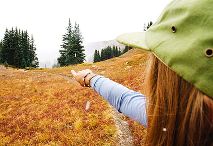 woman pointing hand pine trees field under gray sky thumbnail