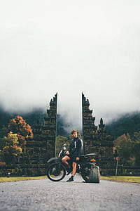 man leaning on motorcycle near trees thumbnail