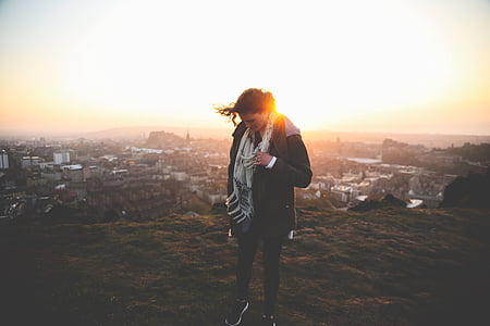 selective focus photography of person standing on cliff near village under golden hour thumbnail