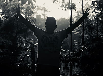Gray Scale Photo of Man in White Shirt Raising His Hand Near Plants thumbnail