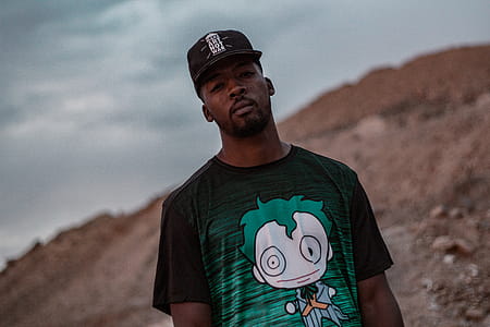 Man in Black and Green Crew-neck T-shirt Standing on Mountain Selective Focus Photography thumbnail
