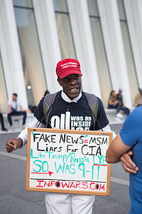 man walking in street wearing fake news MSM liars for CIA signage thumbnail