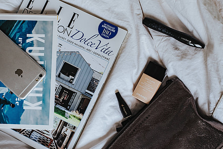 Silver laptop, a camera, magazines and other items on white bed sheets thumbnail