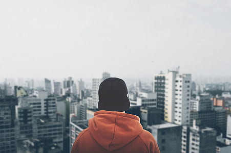 Person Wearing Orange Hoodie Staring at Structural Buildings thumbnail