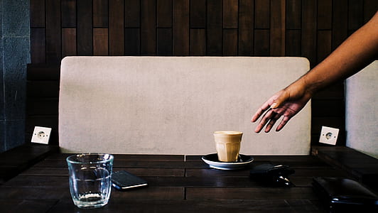 person reaching paper cup on black wooden table thumbnail
