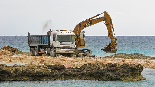 white dump truck beside orange Cat excavator beside body of water at daytime thumbnail